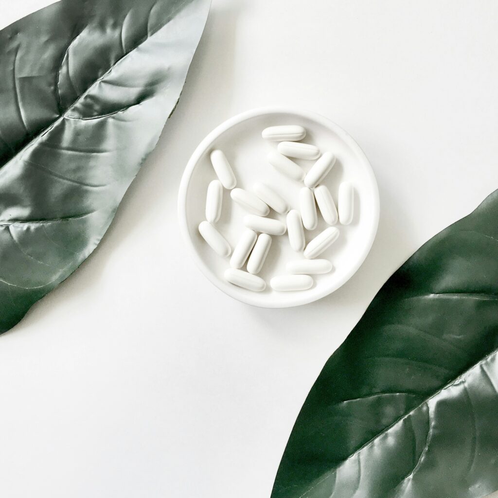 the-tonik-5Lbyao5bzbc-unsplash A white ceramic bowl filled with wellness supplements, surrounded by green leaves on a clean background.